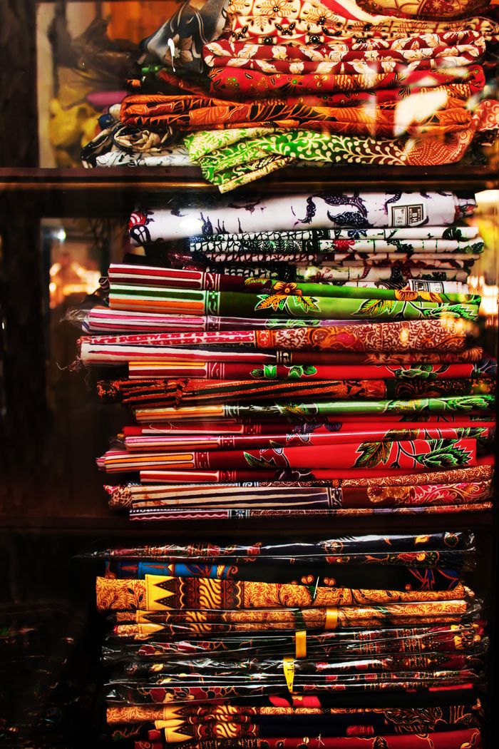 Colorful stack of traditional batik fabrics on a shelf in Malang, Indonesia.